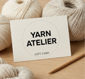 Yarn Atelier gift card with yarn and knitting needles on a wooden surface