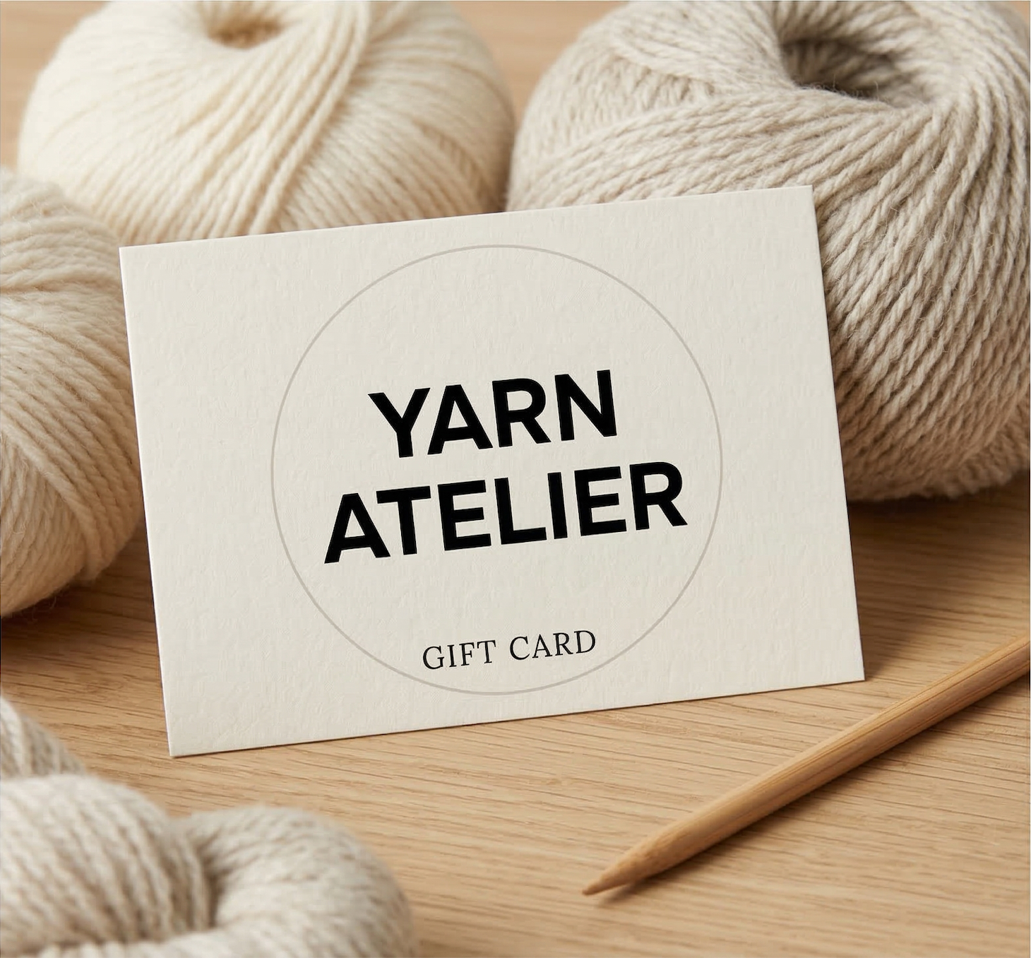 Yarn Atelier gift card with yarn and knitting needles on a wooden surface